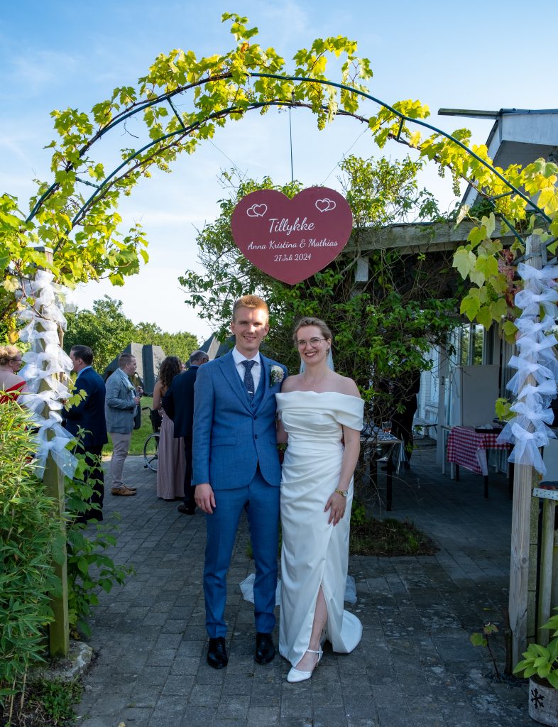 Brudepar under vinranker og hjerteskilt på Vesterhave Vingaard